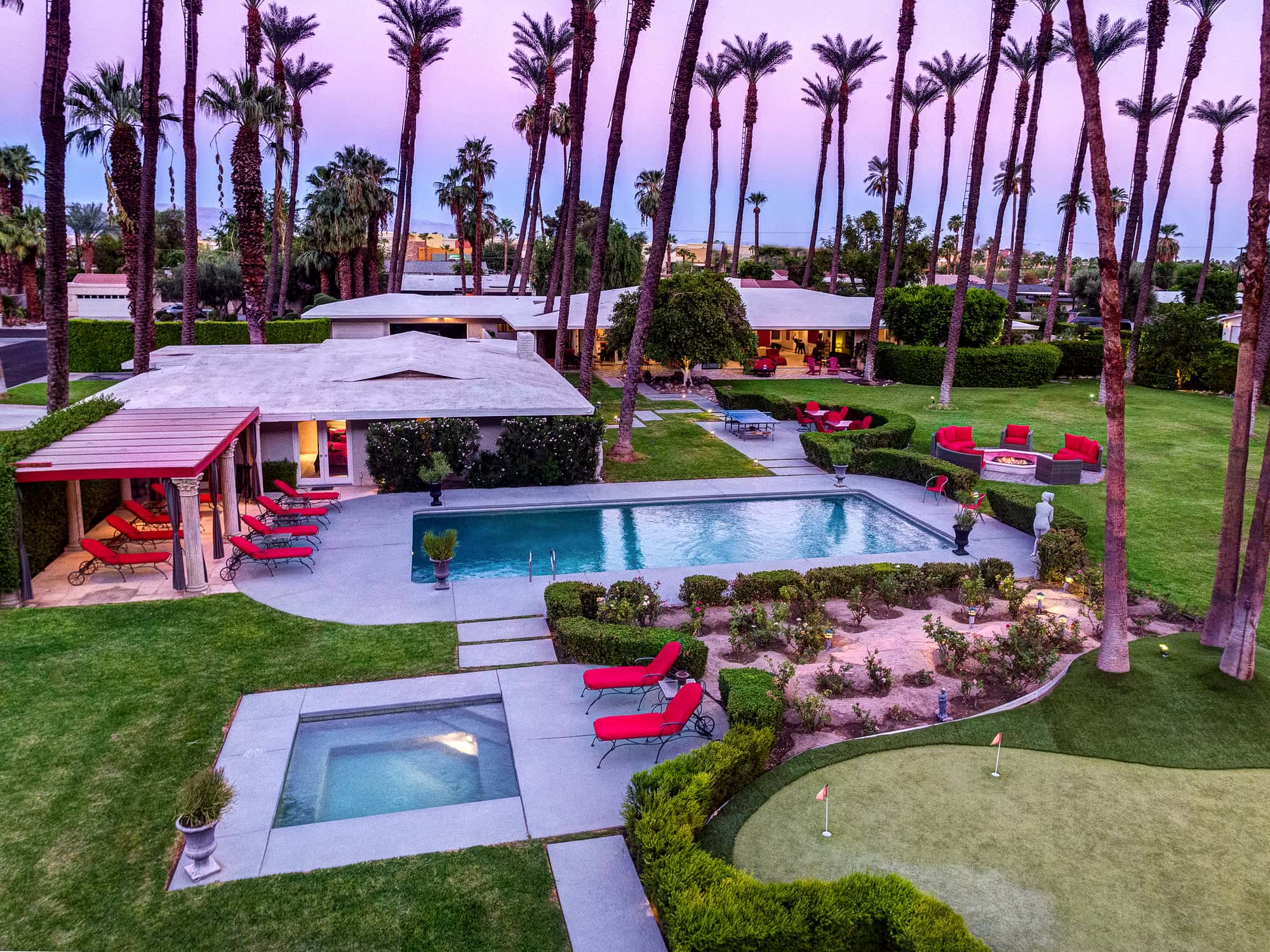 Elevated dusk view over pool, spa, putting green and palm-lined lawn