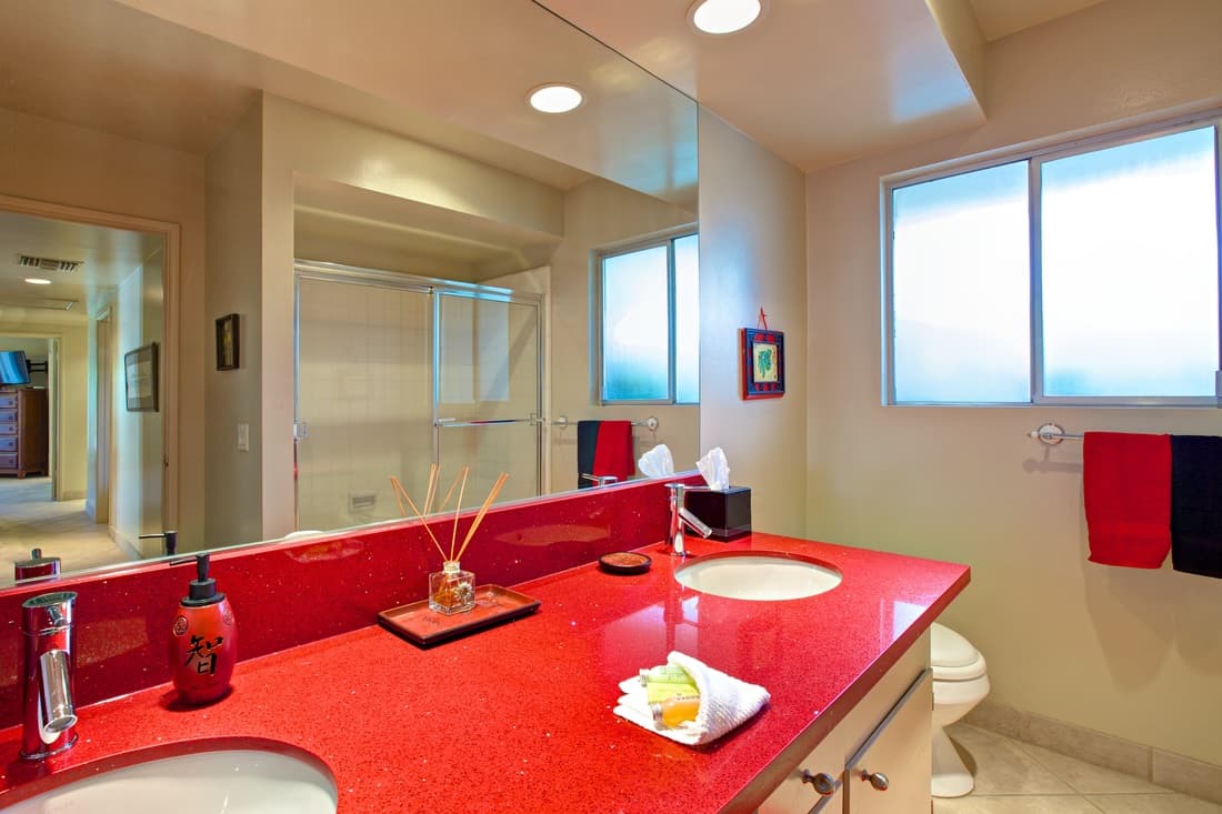 Bathroom with two white sinks set in a red counter, a wide mirror and frosted windows
