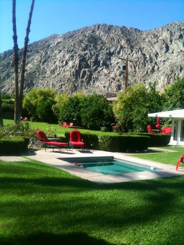 Red lounge chairs beside a small pool on a lawn, with hedges and mountains behind