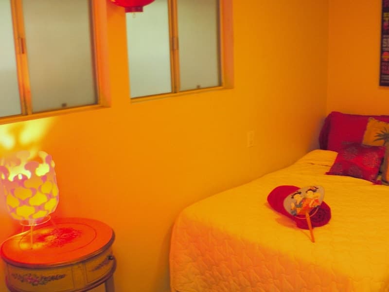 Orange-walled bedroom with frosted windows, a patterned lamp on a painted side table and yellow bedding