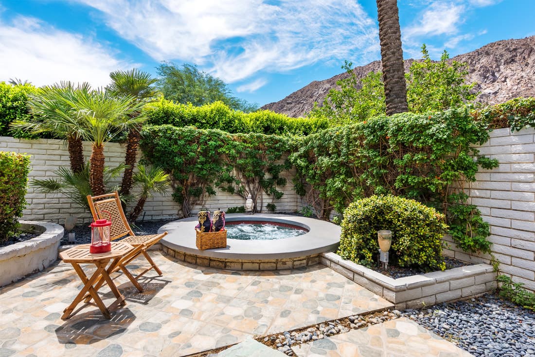 Round sunken jacuzzi in a walled stone courtyard with vine-covered walls, a fan palm and a mountain beyond